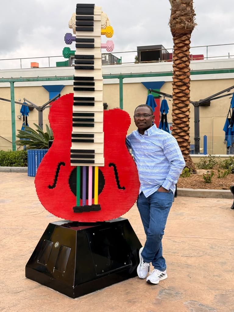 Dr. Nathanael Adjei beside a LEGO guitar sculpture